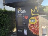 un distributeur automatique sur lequel est posée une pizza, devant un immeuble