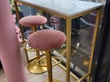 des tabourets de bar roses et dorés et une table au plateau en marbre devant une fenêtre