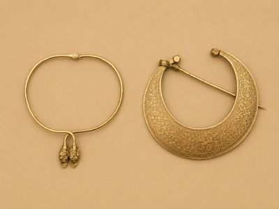 deux bijoux en or posés sur une surface beige