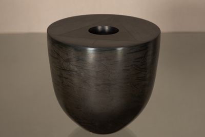 un vase noir posé sur une table, sur fond blanc