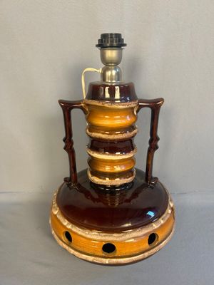 a brown and yellow vase on a stand with a cup on top