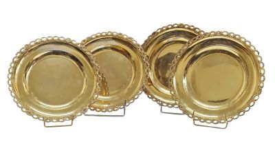 quatre assiettes en or aux bords festonnés, posées sur des socles, sur un fond blanc