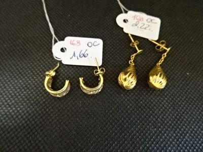 trois paires de boucles d'oreilles en or et une étiquette de prix posée sur une surface noire