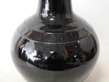 a black vase sitting on a table with a white wall in the background