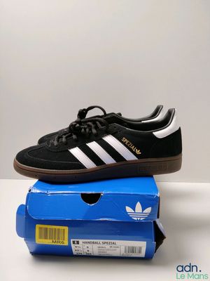 une paire de baskets Adidas noires et blanches posées sur une boîte bleue