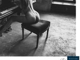 black and white photograph of a naked woman sitting at a piano