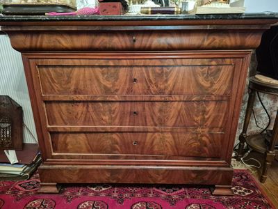 une commode en bois avec un plateau en marbre posée sur un tapis rouge
