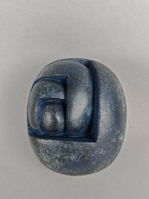 une sculpture représentant un visage, de couleur bleue et blanche, posée sur une surface blanche