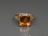 un gros plan d'une bague sertie d'une pierre orange posée sur une surface réfléchissante