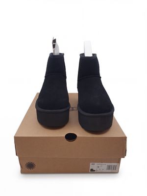 des bottines en daim noir à semelles blanches posées sur une boîte en carton