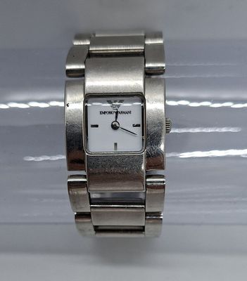 une montre-bracelet en argent avec un cadran blanc posée sur une surface blanche