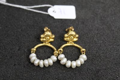 une paire de boucles d'oreilles en or et perles posées sur un fond noir