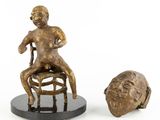 sculpture of a man sitting on a stool next to a head of a man