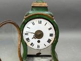 a small green clock with roman numerals on it