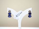 une paire de boucles d'oreilles en verre bleu et argent, posées sur un socle blanc