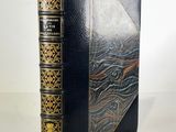 an old book with a black cover and gold trim on a white surface