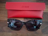 Des lunettes de soleil « Guess » et leur étui posés sur une table en bois