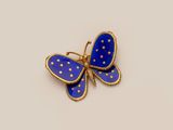 a close up of a blue butterfly broochle on a white surface