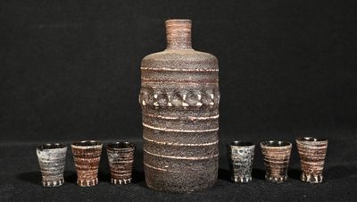 une bouteille et six verres à shot alignés les uns à côté des autres