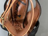 someone is holding a pair of black sandals with a brown strap