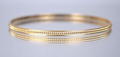 a close up of a gold bang bracelet on a white surface