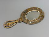 un miroir doré muni d'une poignée dorée et orné d'une rangée de perles bleues et rouges sur le pourtour