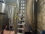 several stainless steel tanks and ladders in a room with a brick wall