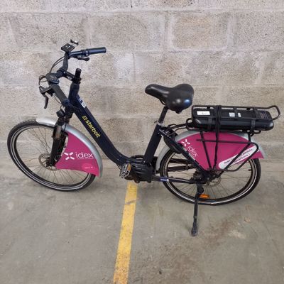 un vélo garé sur un parking, avec un sac rose à l'arrière
