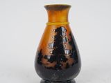 un vase noir et orange posé sur une surface blanche