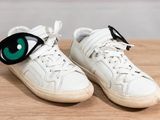 pair of white sneakers with green eyes on them sitting on a wooden surface