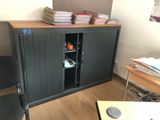 a black cabinet with books on top of it next to a black chair