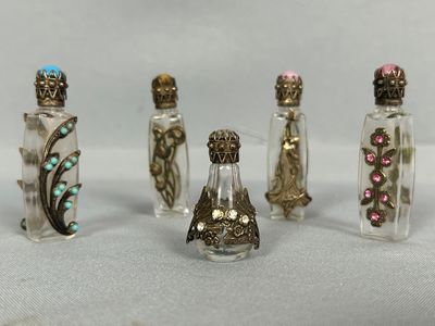 six petites bouteilles dont le verre est de différentes couleurs et ornées de décorations métalliques