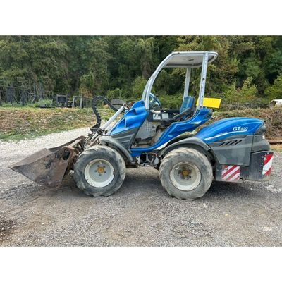 a blue tractor is parked on a gravel road near a forest