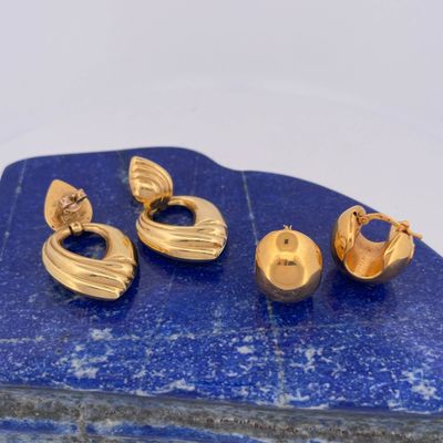 a close up of three pairs of gold earrings on a blue stone
