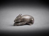 une vieille figurine en argent représentant une souris posée sur une surface grise