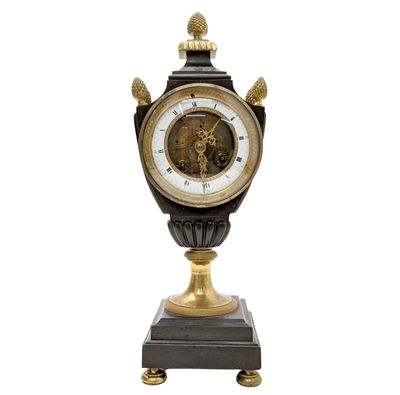 une horloge noire et dorée posée sur un socle, sur fond blanc