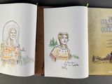 two open books with drawings of native people on them sitting on a table