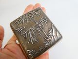 someone is holding a small silver box with bamboo leaves on it
