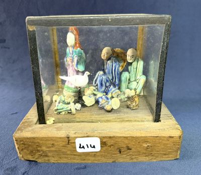 des figurines représentant trois personnes assises dans une vitrine posée sur un socle en bois