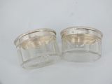 two small glass jars with silver lids on a white surface