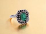 a close up of an emerald and diamond ring on a gold surface