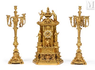 three gold colored candlesticks and a clock on a white background