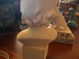 a bust of a woman sitting on a table next to a vase