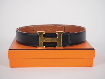 une ceinture noire ornée d'une boucle dorée, posée sur une boîte orange