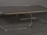 une table en métal avec un plateau en verre posée sur une surface grise