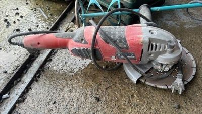 une meuleuse électrique rouge et noire posée par terre
