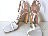 pair of white high heeled sandals with gold accents on a white surface