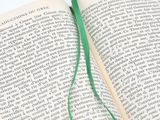 an open book with a green bookmark sticking out of it ' s cover