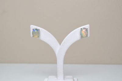 une paire de boucles d'oreilles « oplite » posées sur un socle blanc, sur une table