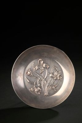 an antique silver plate with flowers on it on a black surface